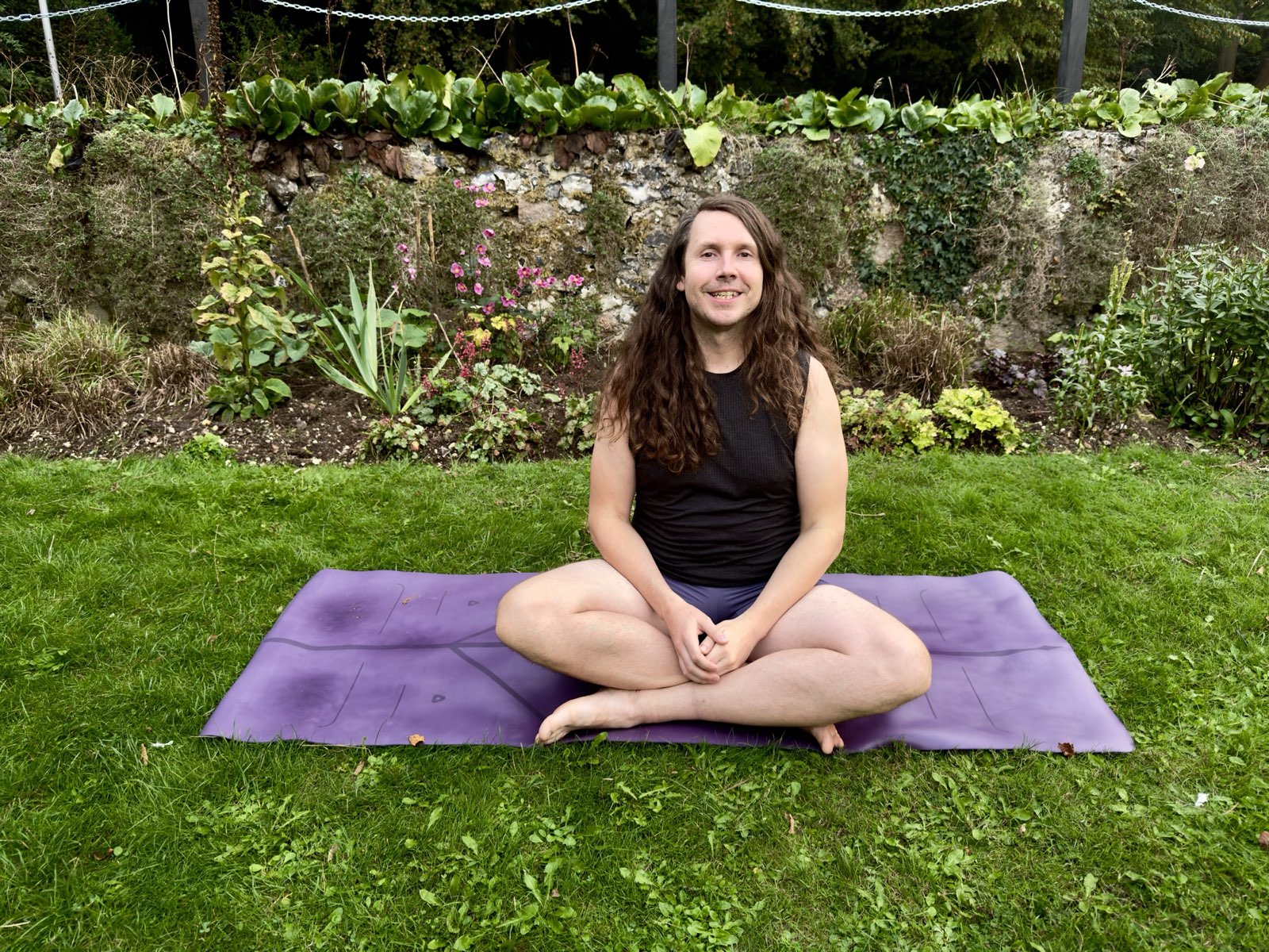 Ben seated cross-legged and smiling on a yoga mat